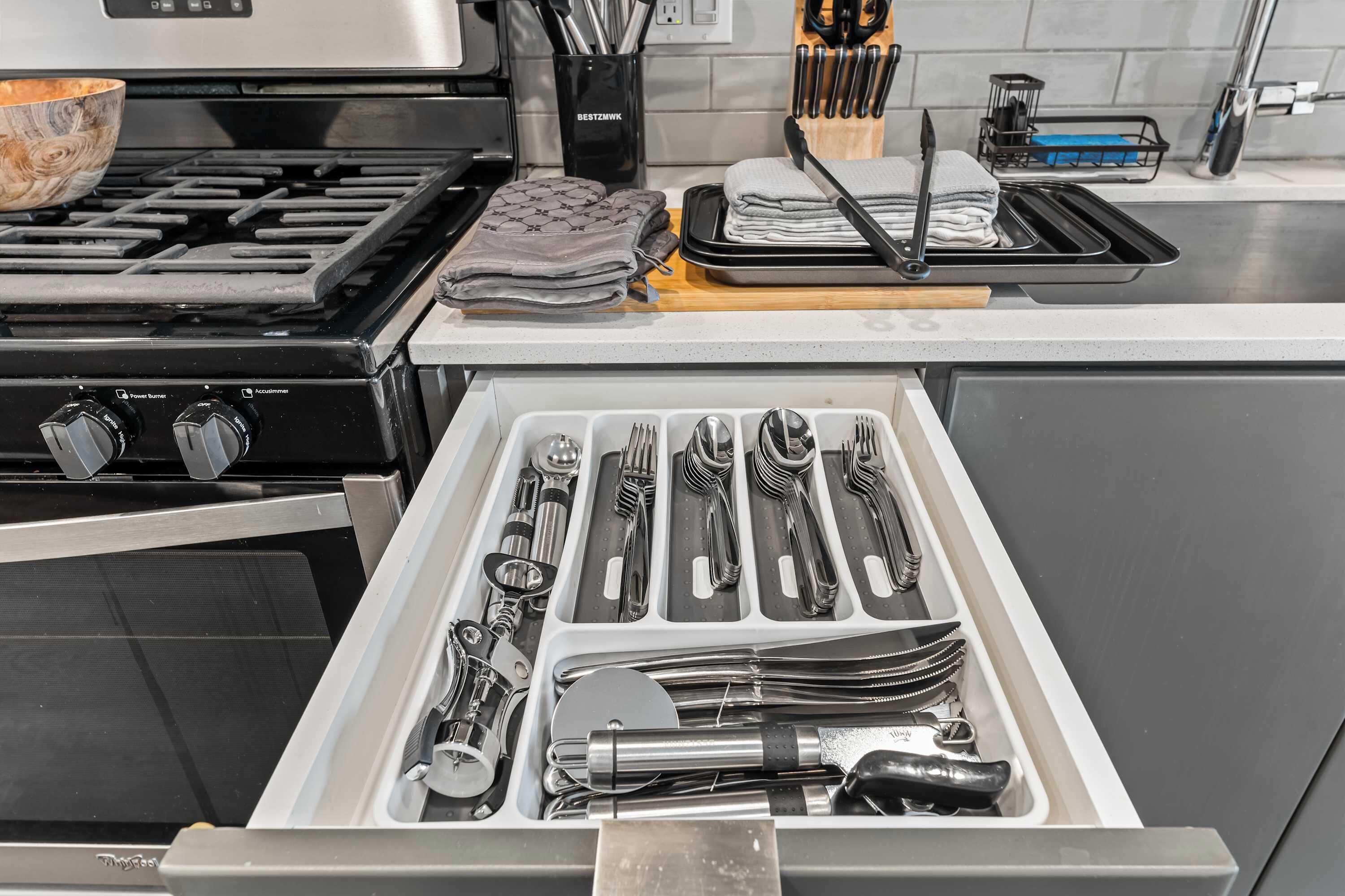 A kitchen with a stove, a drawer with utensils, and a countertop with a cutting board and knives.