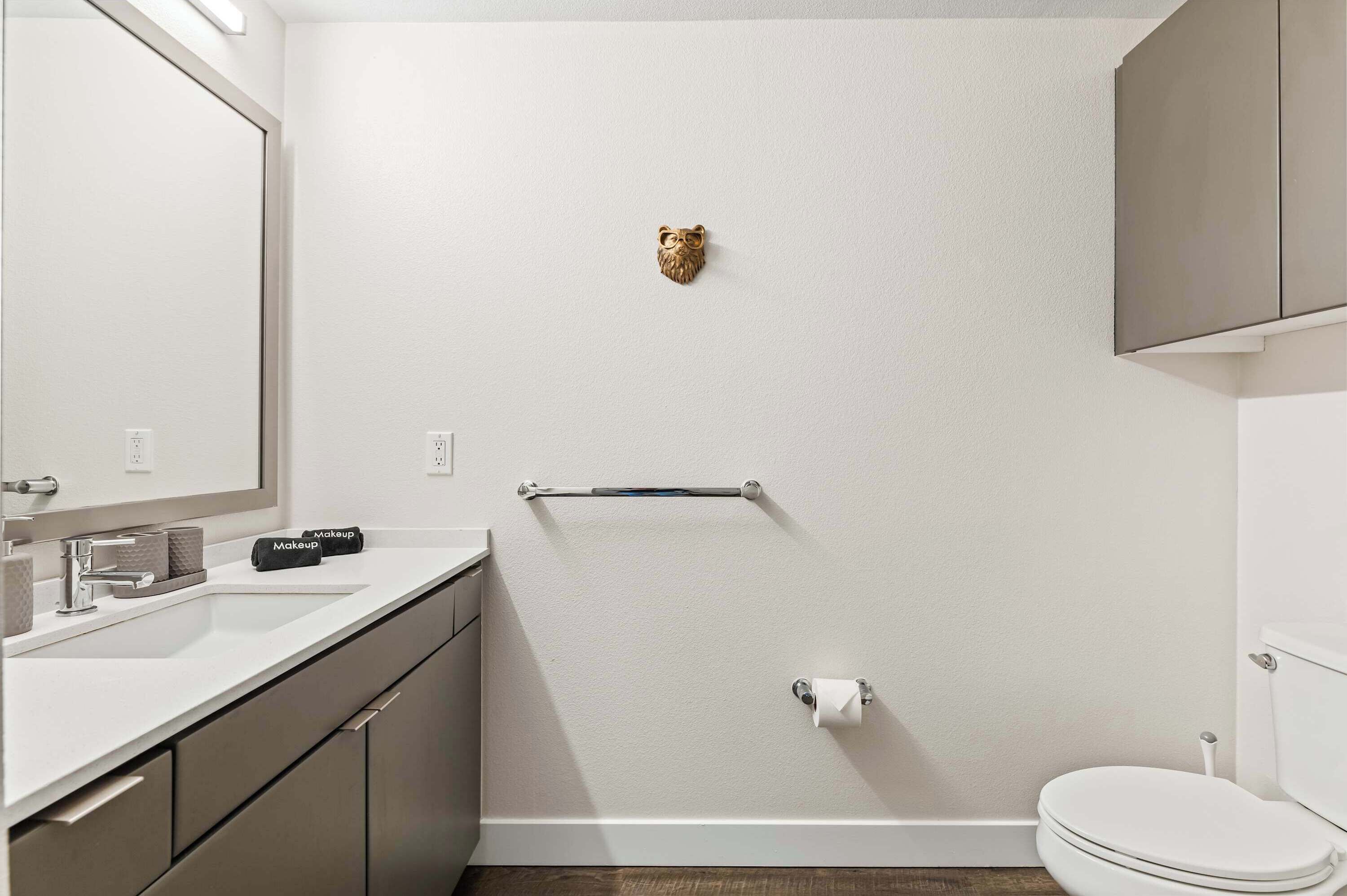 A modern bathroom with a white sink, a mirror, a toilet, and a towel rack.