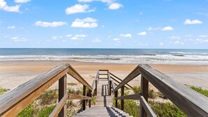 Un escalier en bois menant à une plage, avec un ciel dégagé.