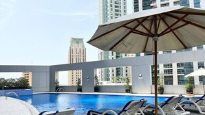 A rooftop pool area with lounge chairs and umbrellas, surrounded by high-rise buildings. - Skyview Tower (Dubai)