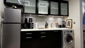A modern kitchen with black cabinets, a stainless steel refrigerator, a coffee maker, and a washing machine. - Skyview Tower (Dubai)