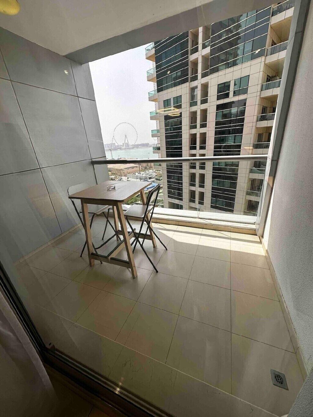 Un balcón con mesa y sillas, una vista de noria y un edificio moderno al fondo.