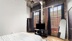 Un dormitorio con cama, televisor, espejo y pared de ladrillo.