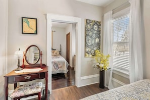 A bedroom with a bed, a dresser with a mirror, a vase with flowers, and a map on the wall.