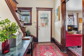A wooden staircase leading to a white door with a stained glass window, a red sofa, and a television in a living room.