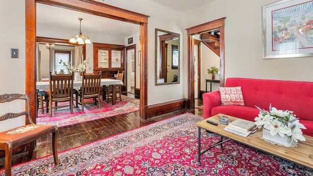A dining area with a wooden table, chairs, and a chandelier. There is a red sofa and a coffee table with a book and flowers. - Downtown Sturgeon Bay Treasure (Sturgeon Bay)