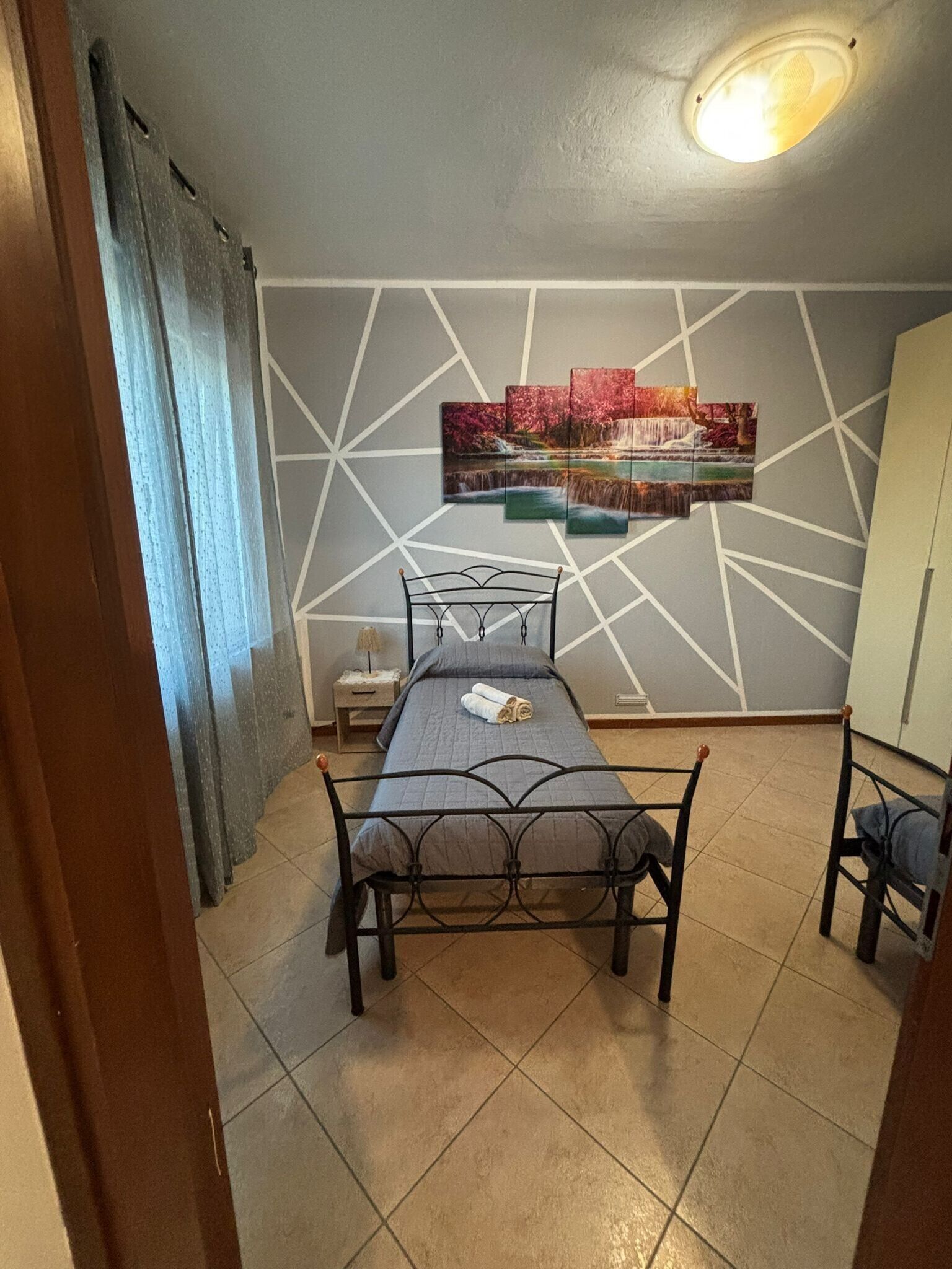 Ein Schlafzimmer mit Bett, Nachttisch, Wandbild und Deckenleuchte.