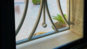 Janela com grade metálica decorativa e vista para um jardim com diversas plantas e flores.