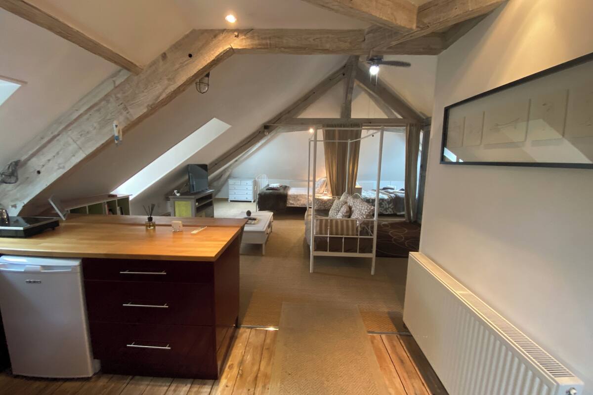 A cozy attic bedroom with a wooden ceiling, a bunk bed, a desk with a computer, and a small refrigerator.