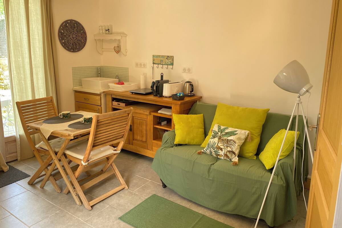 A compact living space with a dining area, kitchenette, and a green sofa with yellow cushions.