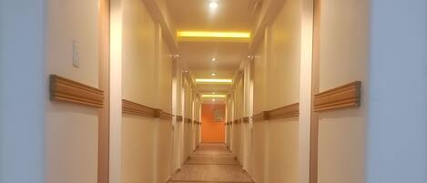 Ein langer, schmaler Hotelgang mit Holzboden und eingelassener Beleuchtung.