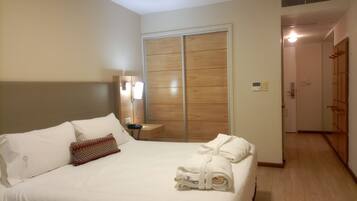 Habitación de hotel con cama, mesita de noche con lámpara, armario de madera y baño a la vista a través de una puerta abierta.