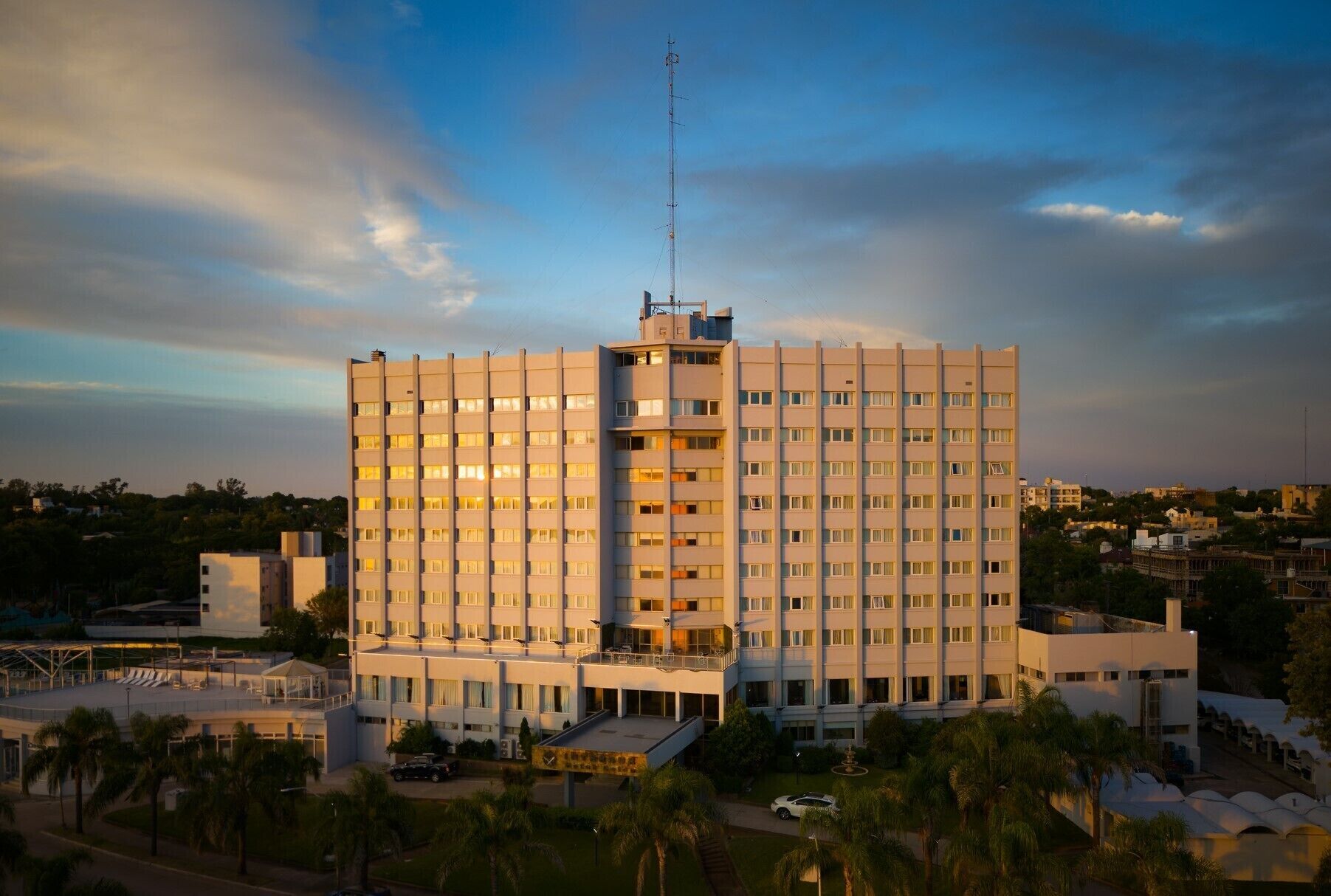 A multi-story hotel with a central tower, balconies, and a parking area.