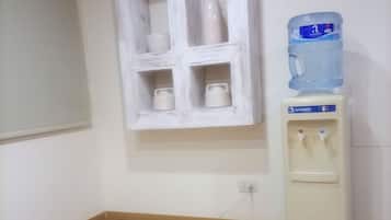 Una stanza con un armadio bianco dotato di quattro ripiani, un dispenser d'acqua e una presa elettrica a parete.