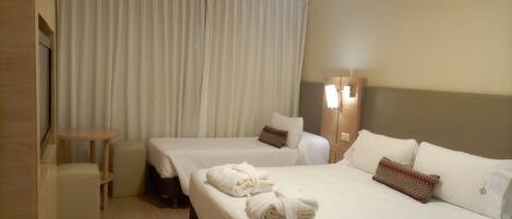 A hotel room with two beds, a small table, a mirror, and a wardrobe.