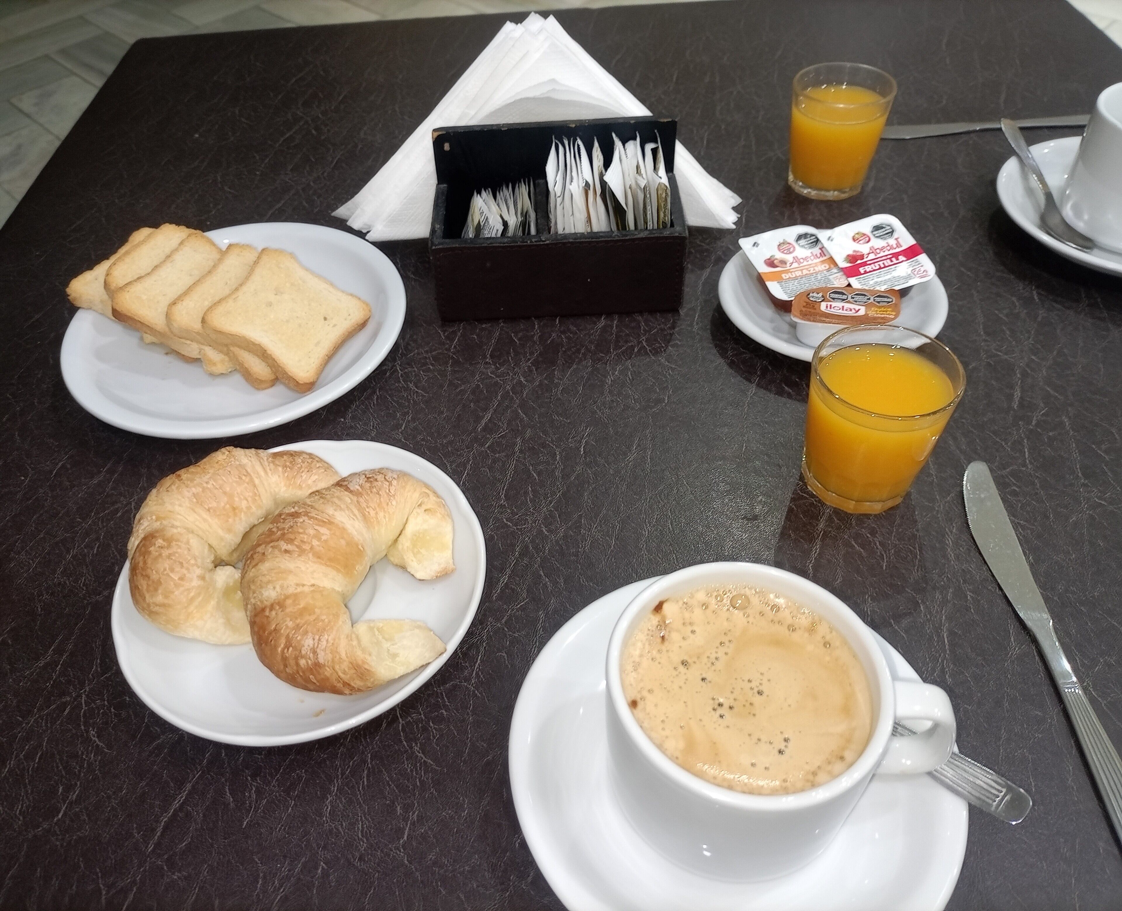 A breakfast setting with croissants, toast, juice, and coffee on a table.