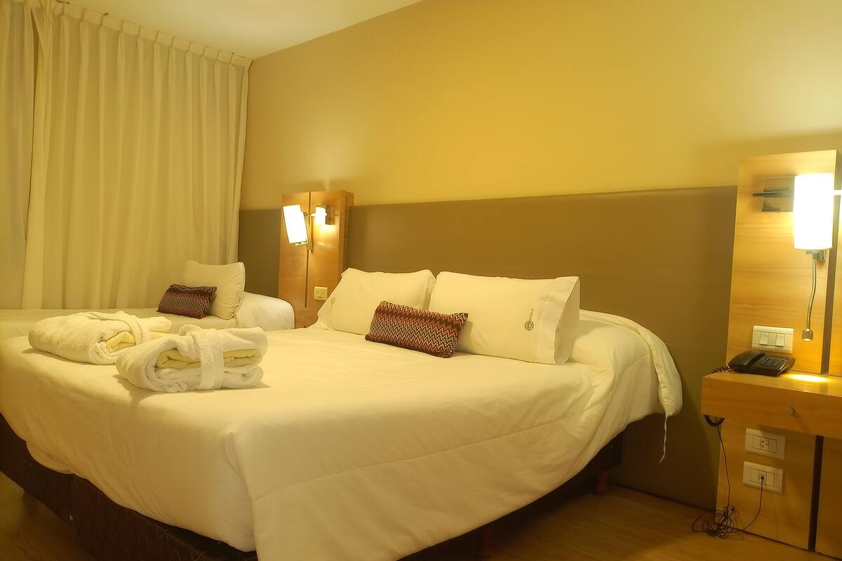 Ein Hotelzimmer mit einem großen Bett, zwei Nachttischlampen, einem Nachttisch mit Telefon und einem Vorhang.