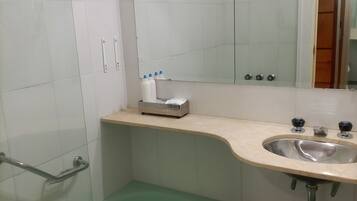 Un baño con una bañera verde, un lavabo con dos grifos, un espejo sobre el lavabo y un estante con artículos de aseo.