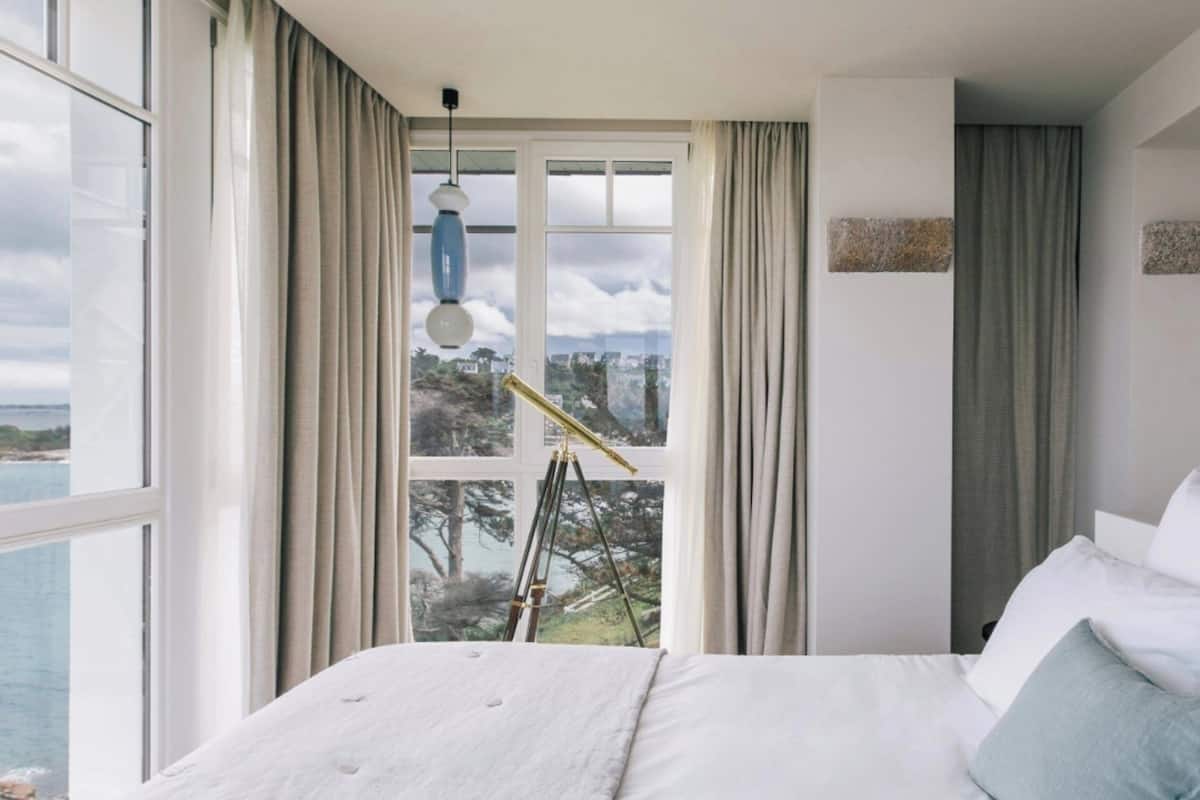 A bedroom with a large bed, a telescope, and a view of the sea.