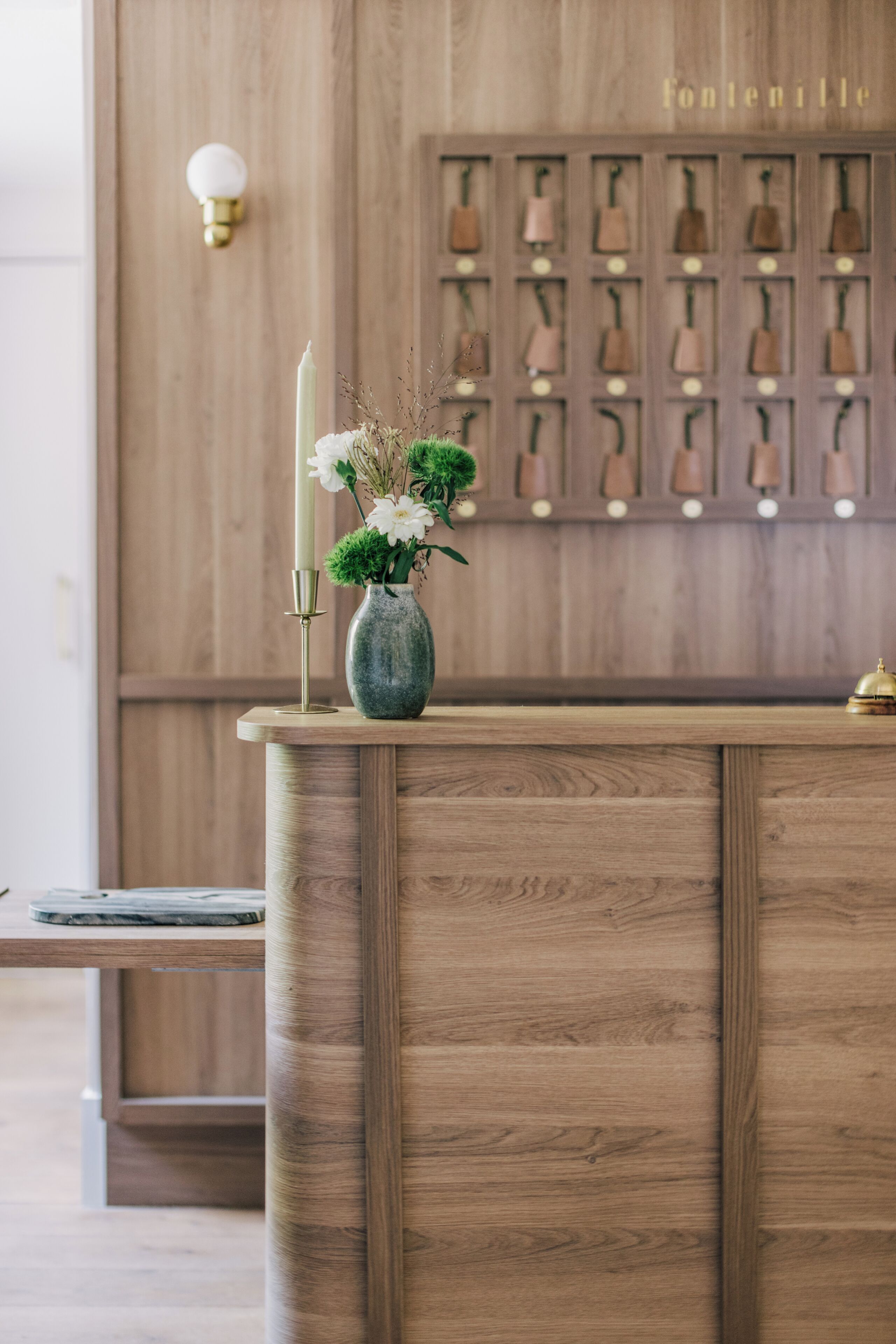 Un comptoir d’accueil en bois, agrémenté d’un vase de fleurs et d’une bougie.
