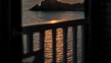 A sunset view through a window with a railing, overlooking a body of water and a distant landmass.