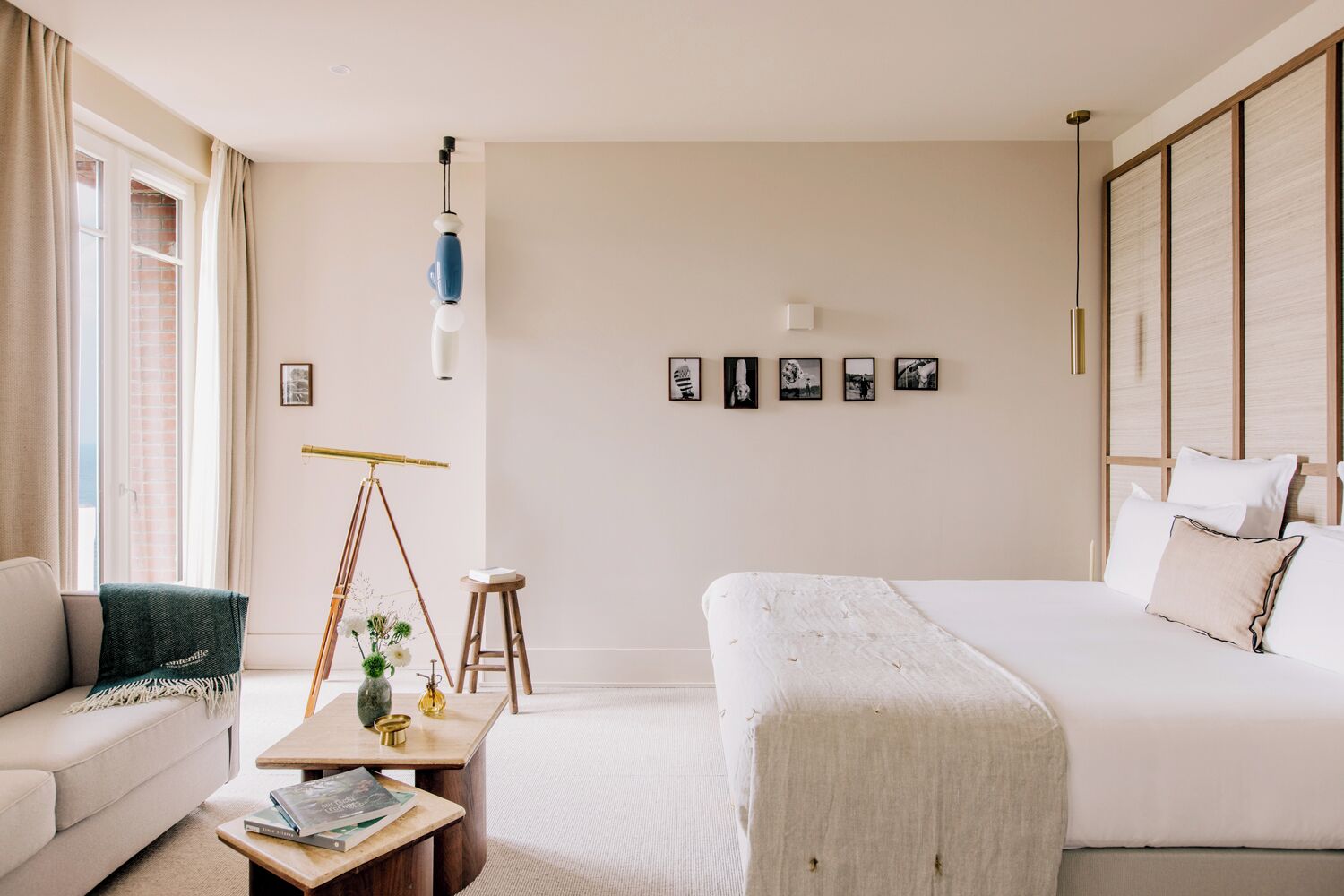 A modern hotel room with a bed, a sofa, a small table, a tripod, and a wall-mounted lamp.