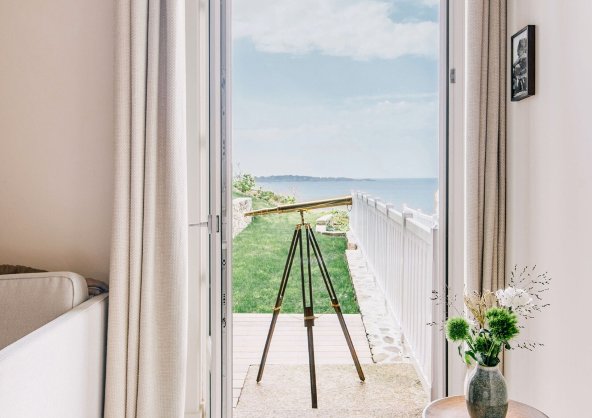 Un balcon avec un trépied, un vase rempli de fleurs et une vue sur la mer.