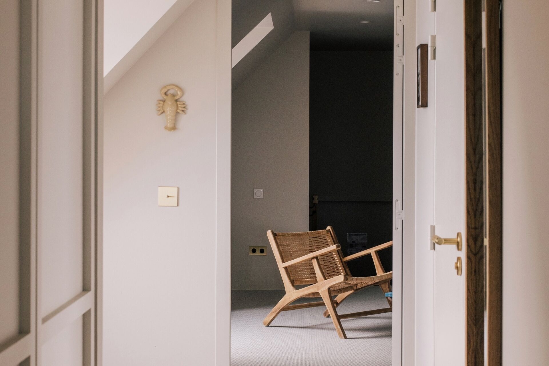 Una stanza con una sedia in legno, un interruttore della luce e un punto luce a parete.