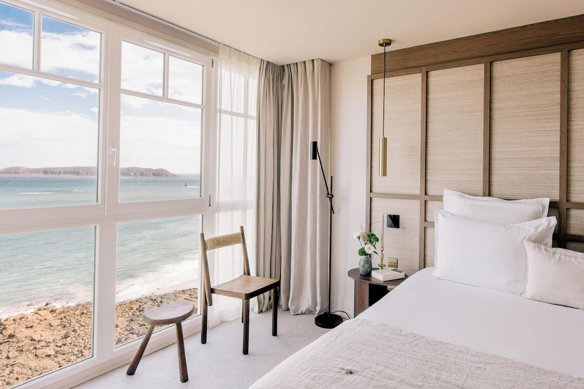 A hotel room with a large window, a bed, a chair, a nightstand, and a lamp.