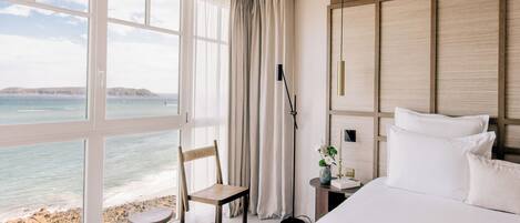 A hotel room with a large window, a bed, a chair, a nightstand, and a lamp.