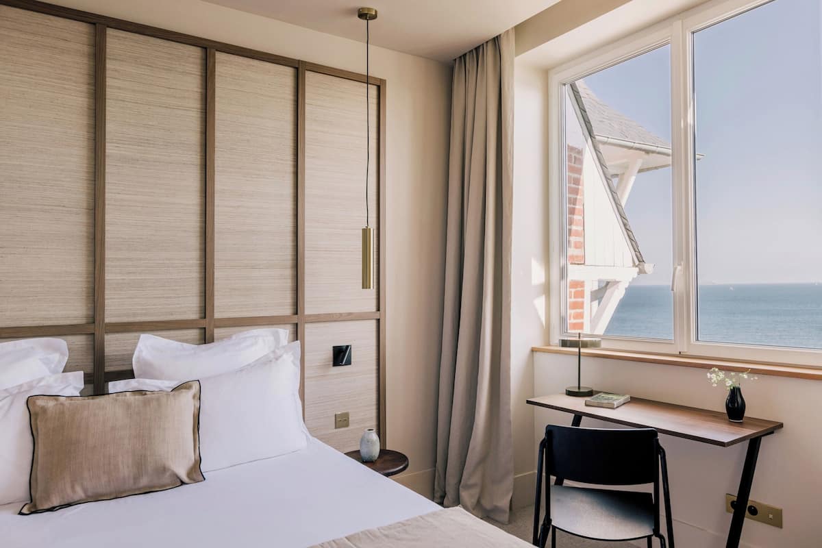A hotel room with a bed, a desk, and a view of the sea.