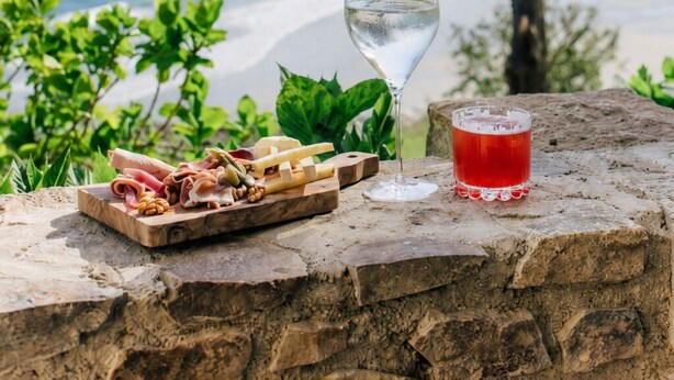 A stone ledge with a glass of white wine, a glass of red drink, and a wooden board with food. - Les Bassans - Fontenille Collection (Perros-Guirec)