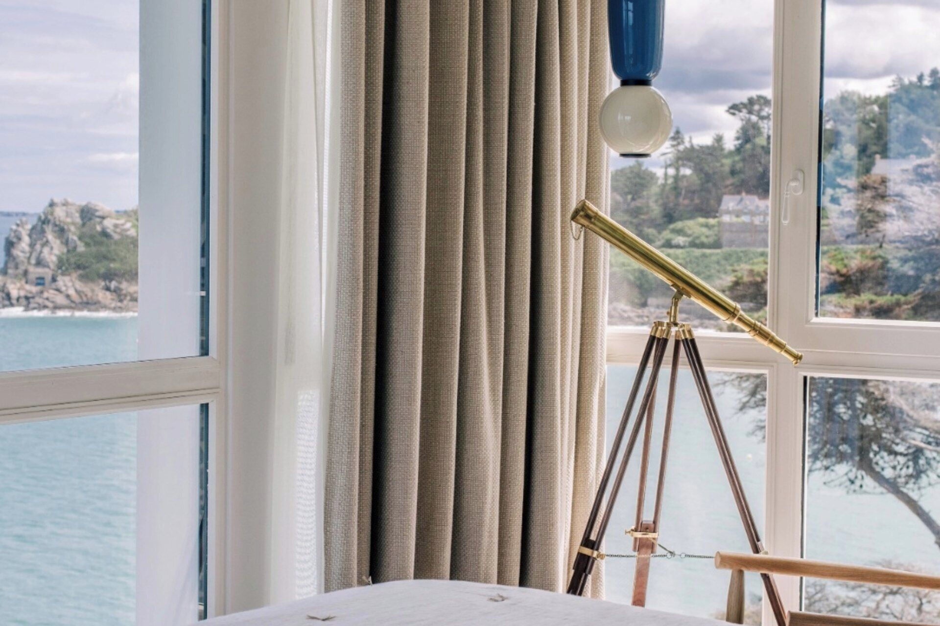 A room with a large window, curtains, and a telescope.