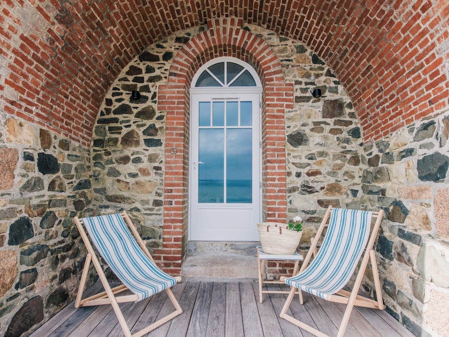 A stone-walled room with a white door, two striped beach chairs, and a basket on the floor.