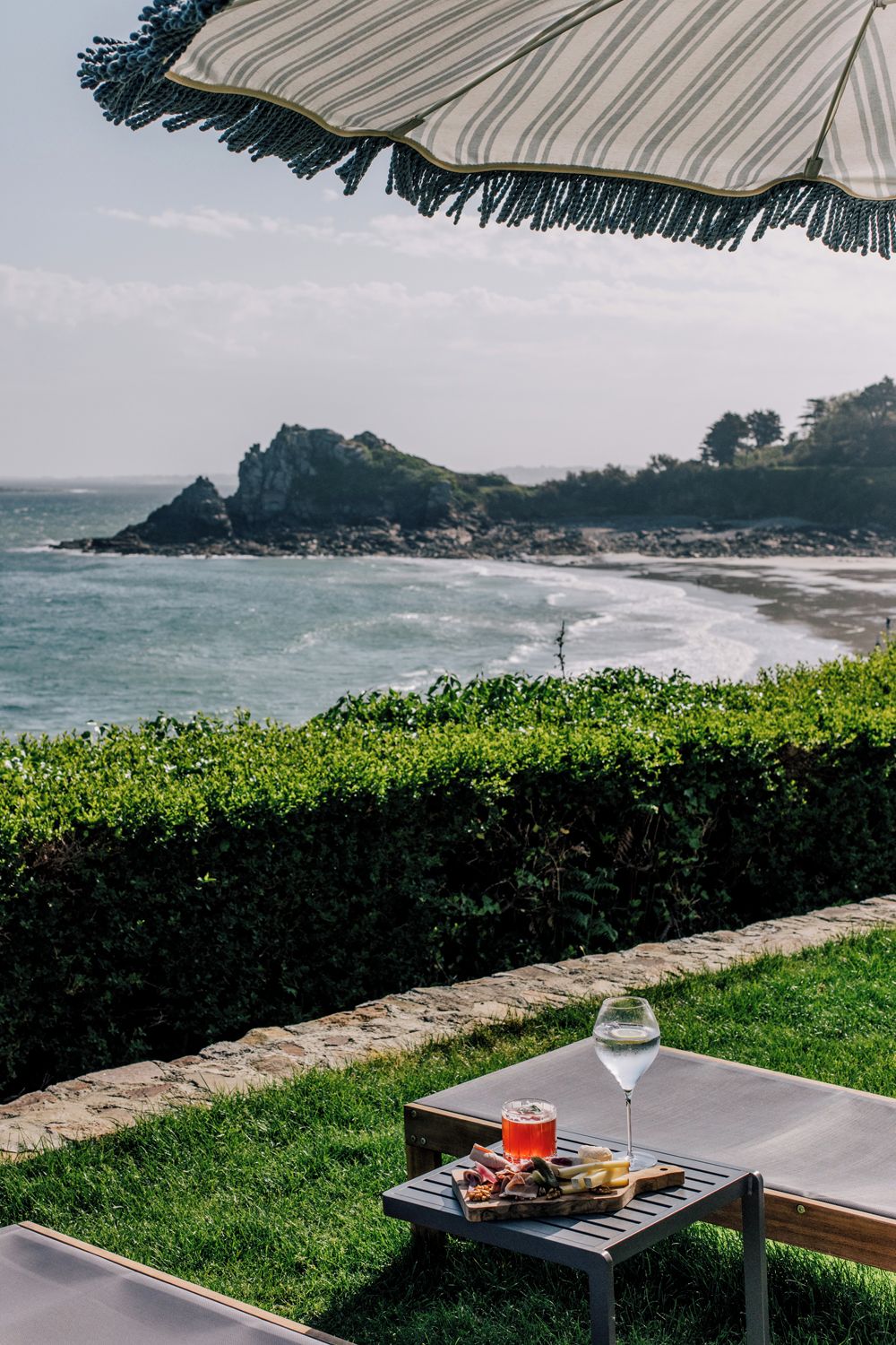 Un espace de restauration en plein air avec une table dressée pour deux personnes, un verre de vin blanc et une planche de charcuterie.
