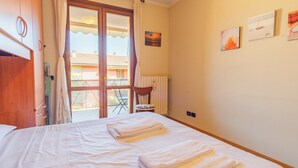 Un dormitorio con cama, una silla, un ventanal con cortinas y vistas al exterior.