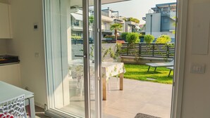 Eine moderne Wohnung mit einer Schiebetür zu einem Balkon. Der Balkon bietet einen Tisch mit Stühlen, eine kleine Grünanlage mit Pflanzen und Blick auf umliegende Gebäude.
