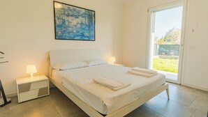 Ein Schlafzimmer mit einem Bett, zwei Nachttischen mit Lampen, einem Bild an der Wand und einer Glastür zu einem Balkon.