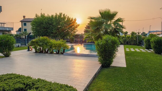 Ein Poolbereich mit Sonnenuntergangsblick, umgeben von Grünflächen und einem gepflasterten Weg.