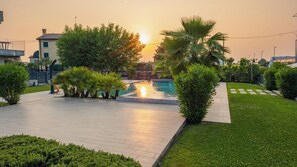 A pool area with a sunset view, surrounded by greenery and a paved walkway.