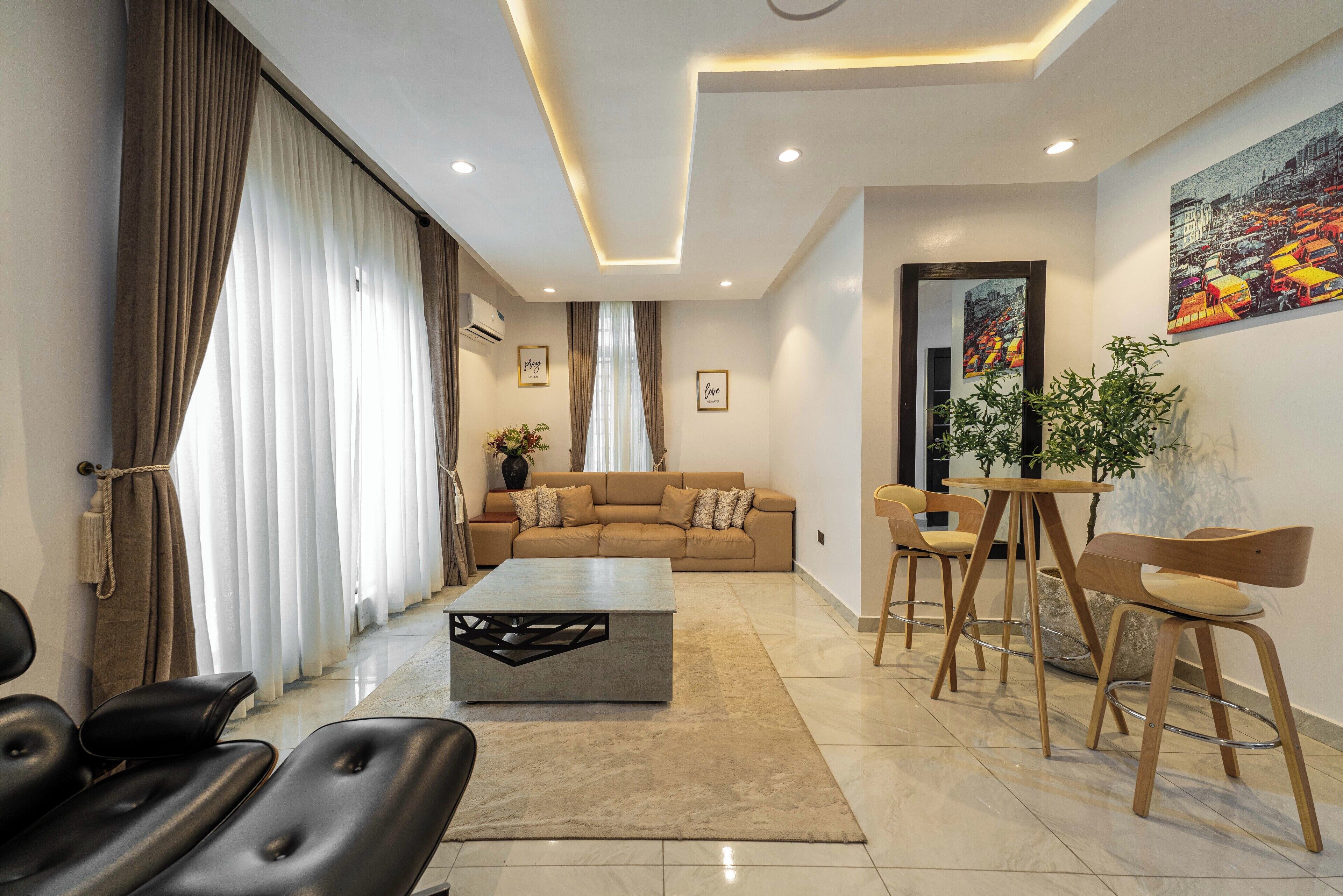 Una sala de estar moderna con un sofá, una mesa de centro y sillas. Hay un cuadro en la pared y una planta sobre una mesa.