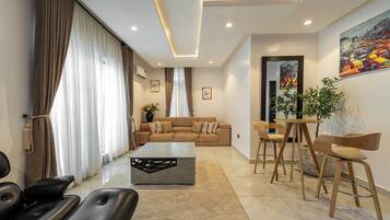Una sala de estar moderna con un sofá, una mesa de centro y sillas. Hay un cuadro en la pared y una planta sobre una mesa.