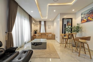 A modern living room with a sofa, coffee table, and chairs. There is a painting on the wall and a plant on a table.