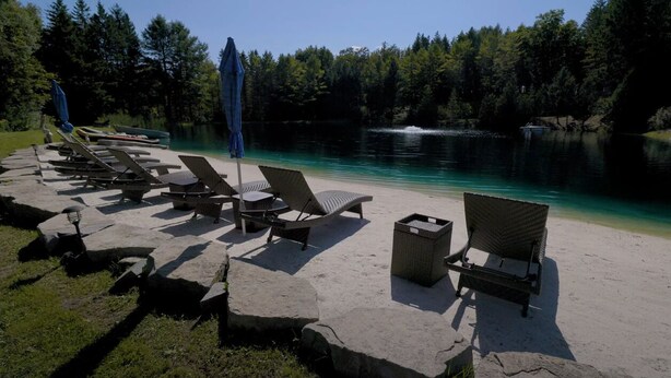 A lakeside lounge area with lounge chairs and umbrellas, surrounded by trees and a clear view of the lake. - Cozy Bunkie by a Tranquil Freshwater Pond in Clarington, Ontario (Bowmanville)