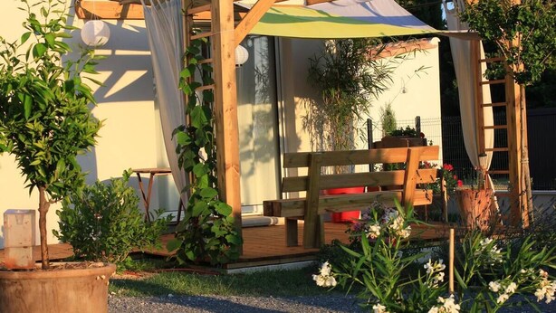 Une structure de pergola en bois, agrémentée d’un banc et d’une table, et entourée de plantes et de fleurs en pot.