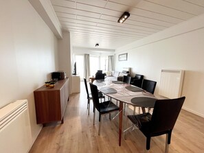 A modern dining area with a long table, chairs, and a wooden cabinet. - Apartment in Wenduine With Sea Views (De Haan)