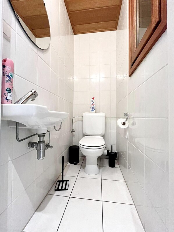 A compact bathroom with a white sink, toilet, and a mirror above the sink. - Apartment in Wenduine With Sea Views (De Haan)