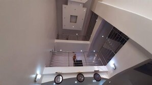 Un interno moderno con una scalinata centrale, un design geometrico del soffitto e una ringhiera in metallo.