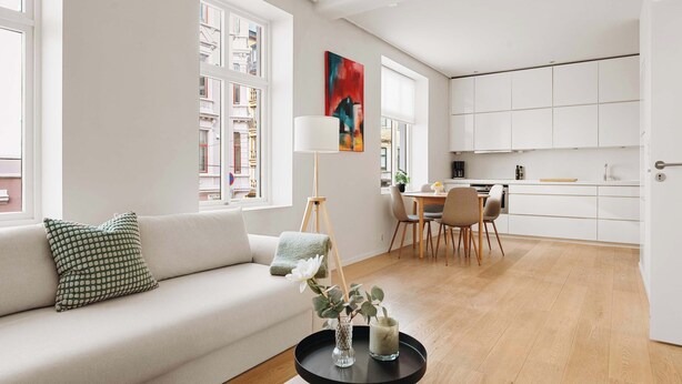Ein modernes Wohnzimmer mit einer Couch, einem Couchtisch mit Dekoration, einem Essbereich mit Stühlen und einer Küche im Hintergrund.