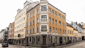 Ein Eckgebäude mit mehreren Stockwerken, das Baustile verschiedener Epochen vereint und eine Vielzahl von Geschäften im Erdgeschoss aufweist.